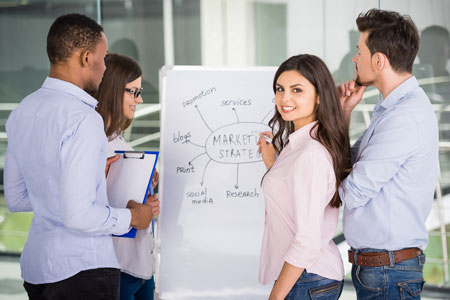 Eine junge Frau schaut in die Kamera und arbeitet zusammen im Team mit anderen Personen an einem günstigen Flipchart